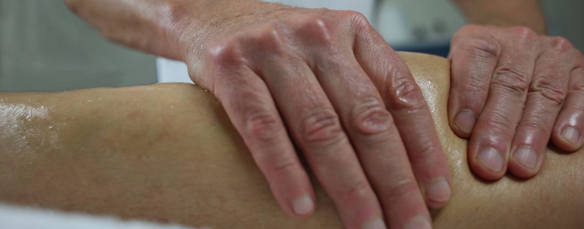 Twee handen masseren de kuit en het bovenbeen van een sporter op de behandeltafel